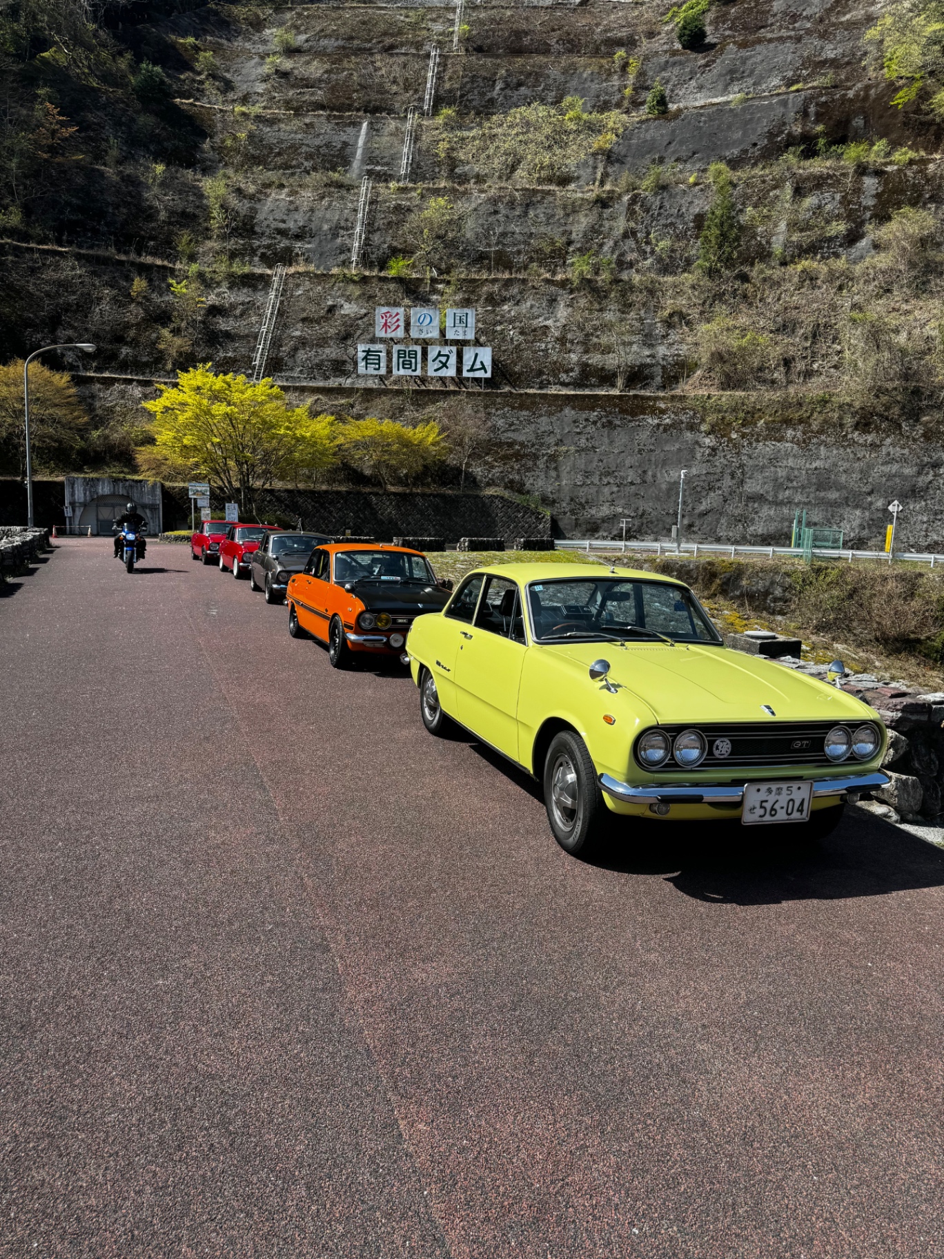 Reihe klassischer Autos vor einer Staumauer in Japan