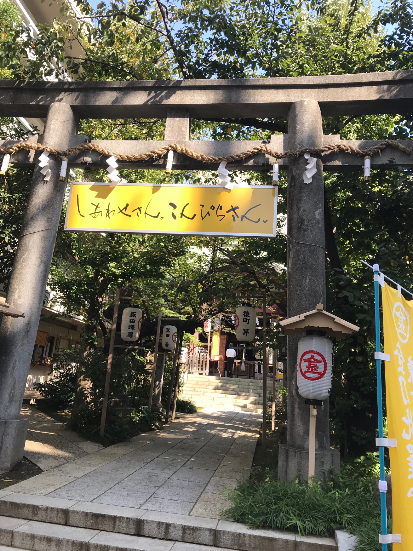 Steinernes Torii mit Shimenawa und gelbem Banner am Eingang eines Konpira-Schreins