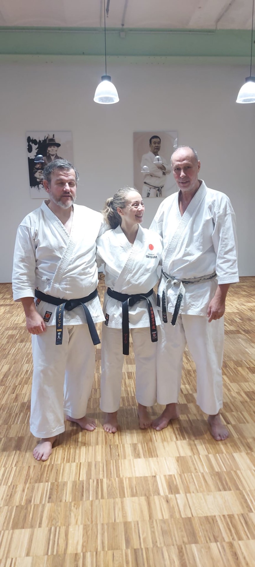 Drei Schwarzgurte im Dojo vor den Porträts der JKA-Meister