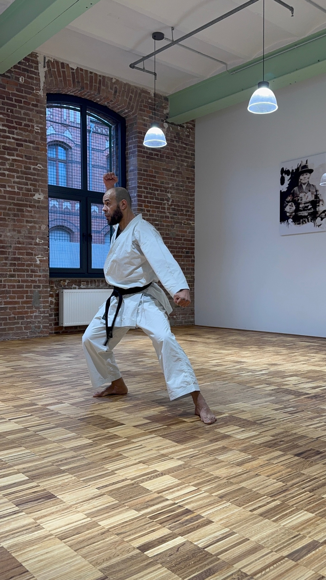 Karateka im hohen Stand vor dem Backsteinfenster des Dojos